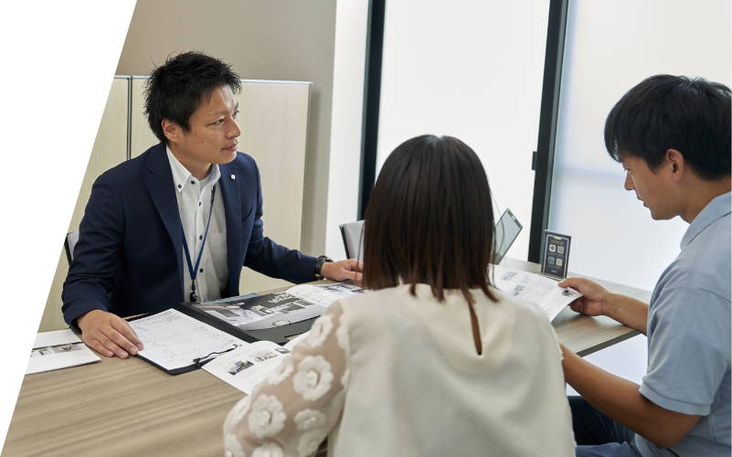 応接室でスーツ姿の男性が、カジュアルな服装の二人と会話する様子。